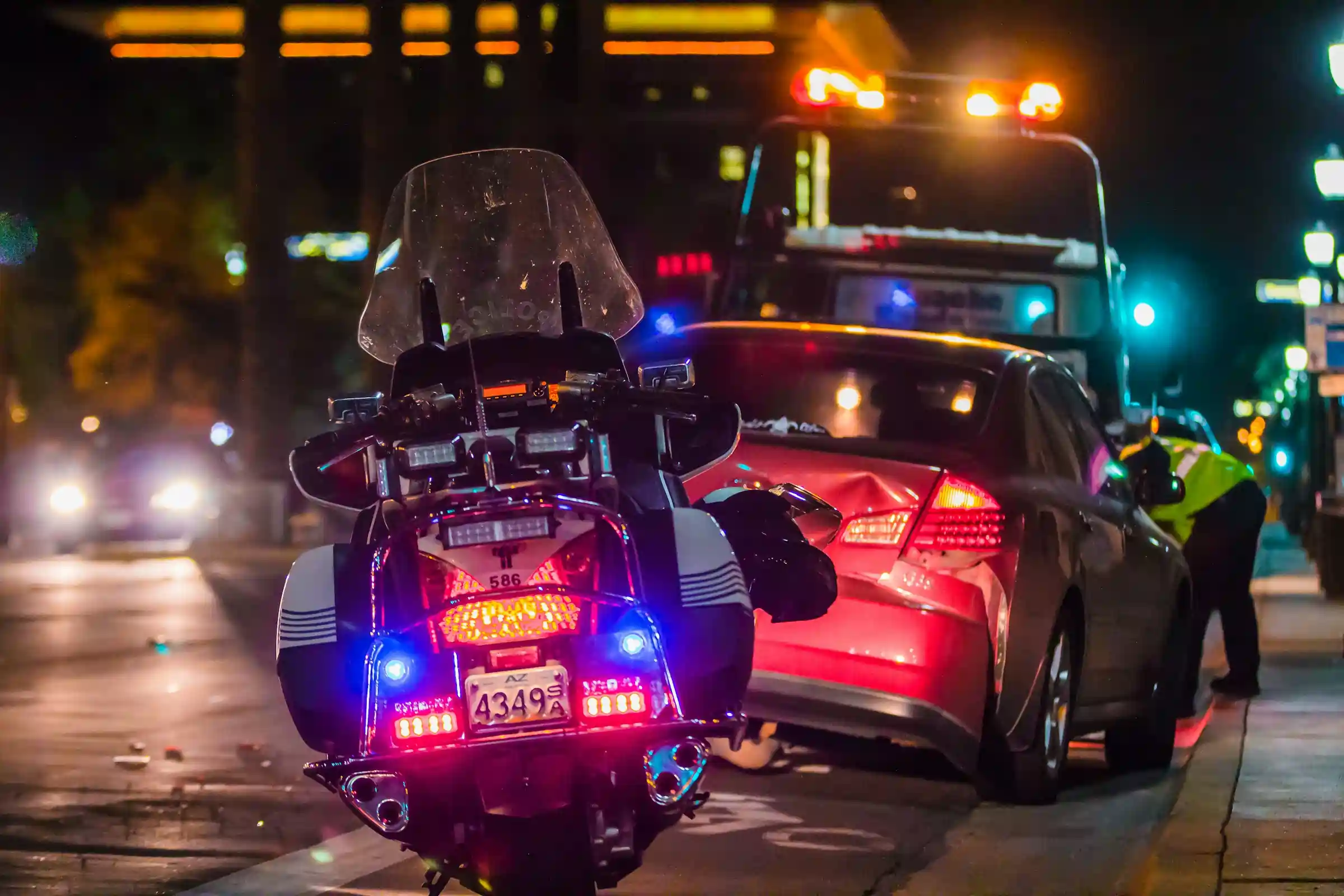 Stovintis policijos motociklas, šalia avariją patyrusio raudonos spalvos automobilio