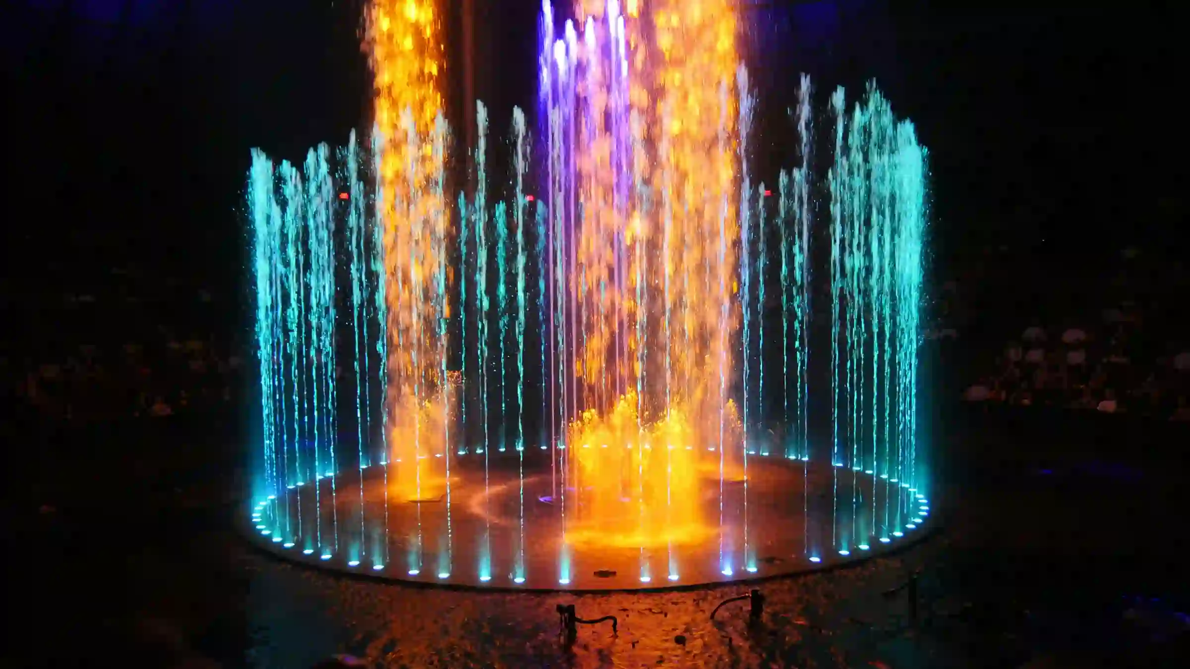 Įvairių spalvų šviečiantis fontanas nakties tamsoje.