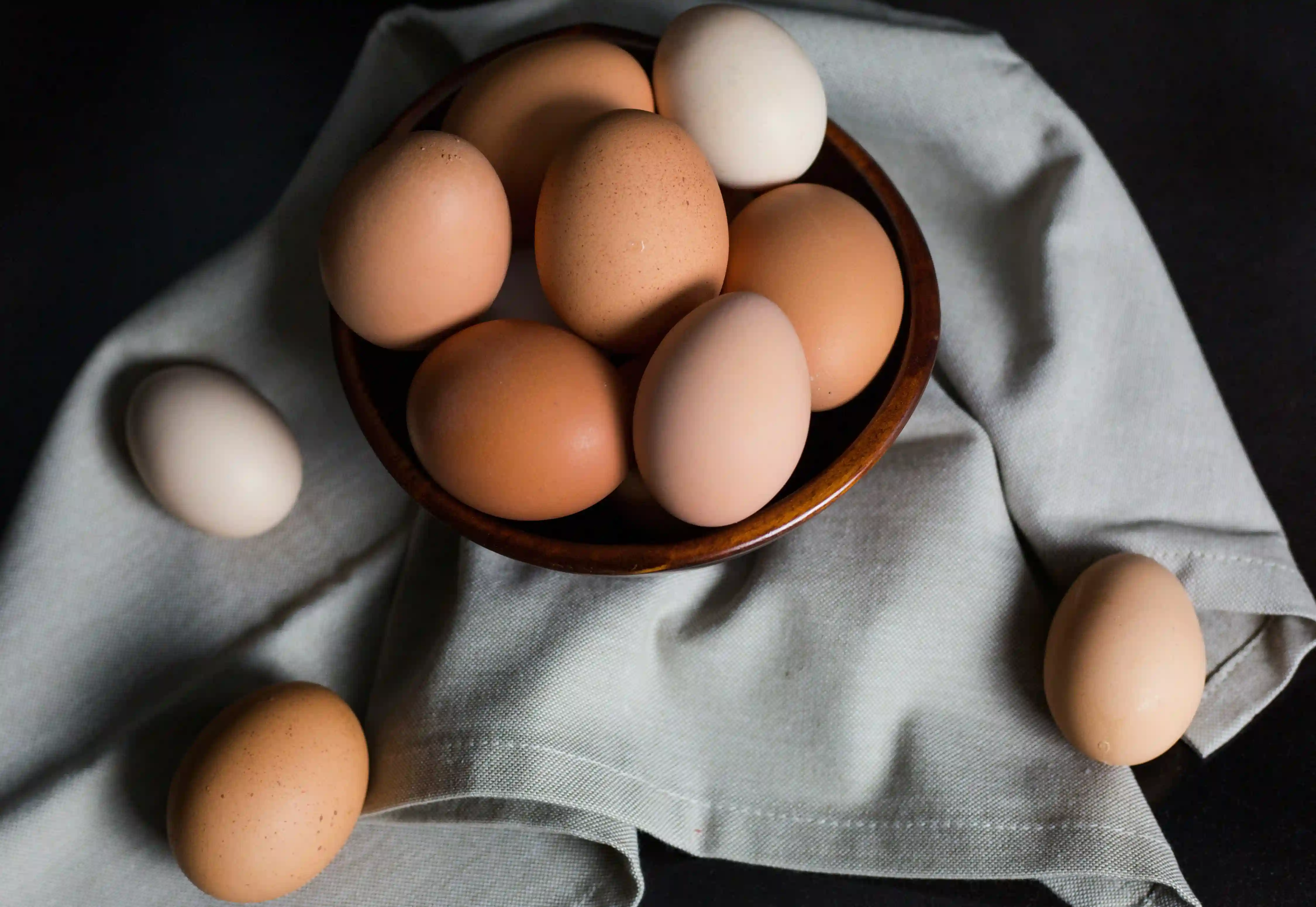 Pilkos spalvos lininė staltiesė ant kurios padėtas rudos spalvos medinis dubuo su kiaušiniais