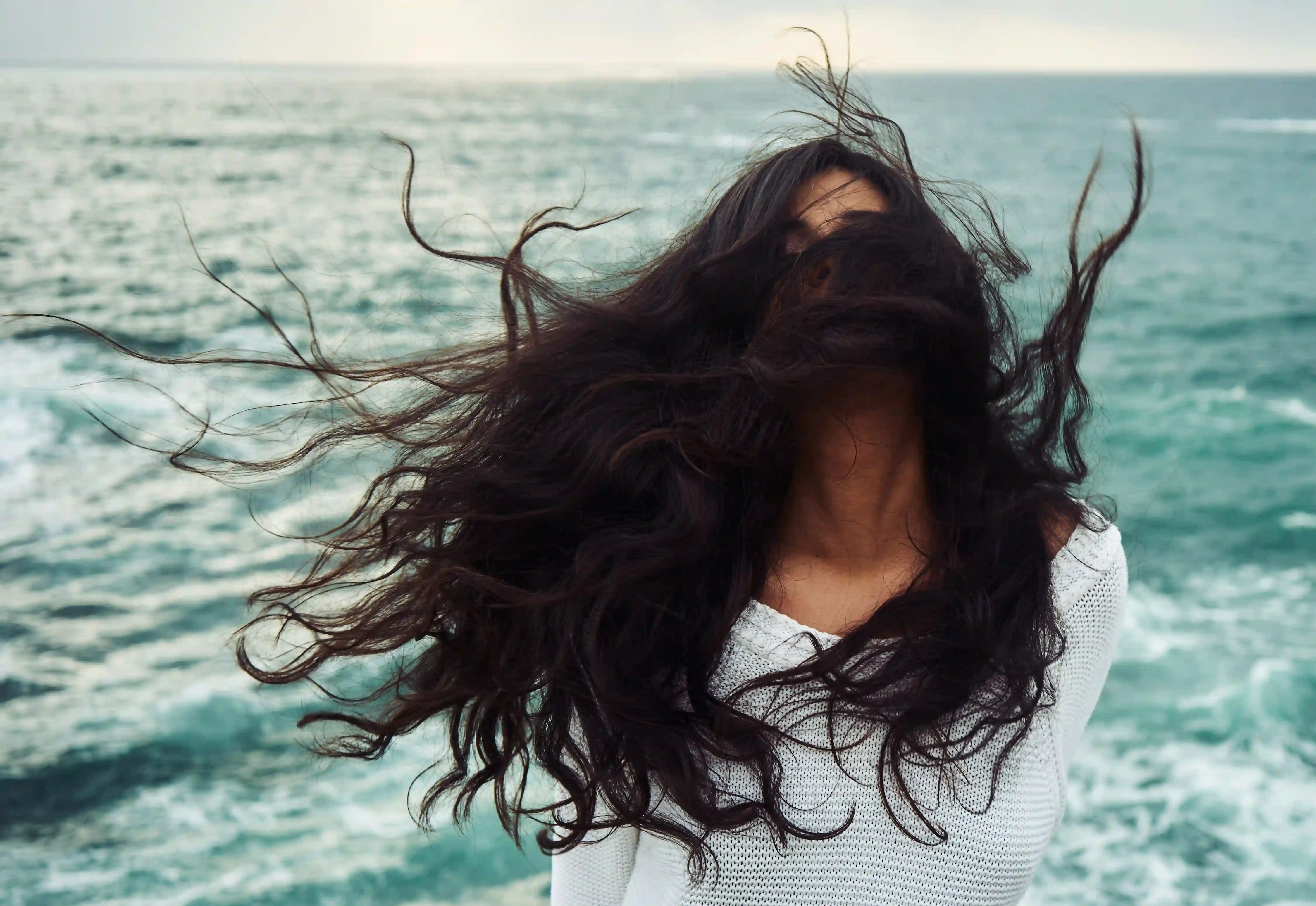Moteris stovi prie jūros vėjas blaško jos juodos spalvos plaukus
